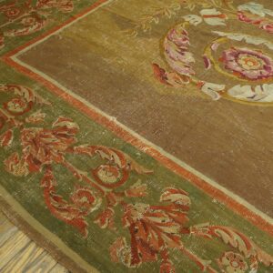 Ornate gold and olive green rug with classical floral patterns rests on aged herringbone wood flooring.