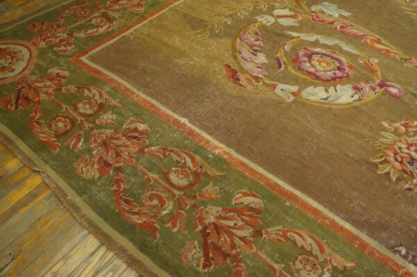 Ornate gold and olive green rug with classical floral patterns rests on aged herringbone wood flooring.