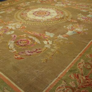 Golden-brown low-pile rug with intricate pink, cream, and red floral designs and a patterned green border.