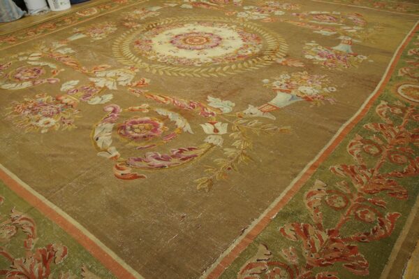 Golden-brown low-pile rug with intricate pink, cream, and red floral designs and a patterned green border.