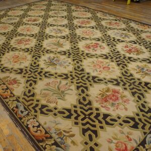 Cream rug with dark trellis and floral motifs in pink, blue, and green on rustic wood flooring.