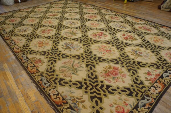 Cream rug with dark trellis and floral motifs in pink, blue, and green on rustic wood flooring.