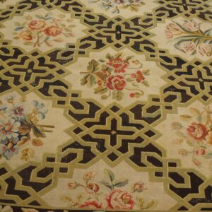 Cream rug featuring dark brown interlocking geometric patterns outlined in olive green, interspersed with colorful floral clusters.