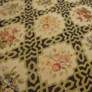 Low-pile cream rug with a dark geometric lattice and olive green trim surrounding colorful floral patterns.