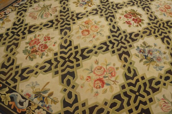 Low-pile cream rug with a dark geometric lattice and olive green trim surrounding colorful floral patterns.