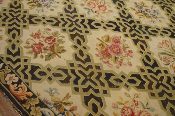 A cream rug displays dark brown interlocking geometric bands framing multicolored floral bouquets on a wood floor.