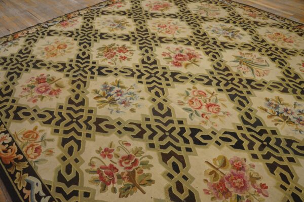 Low-pile beige rug with dark geometric motifs outlined in olive, framing multi-colored floral clusters on plank flooring.