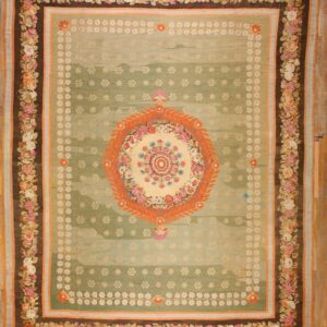 Ornate green rug with an orange medallion and pink rose border lies on light wood flooring.