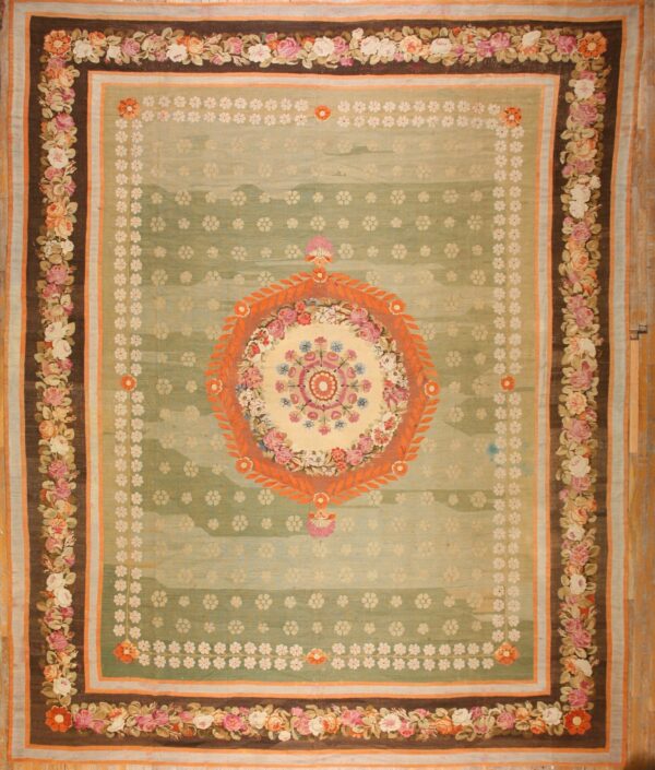 Ornate green rug with an orange medallion and pink rose border lies on light wood flooring.
