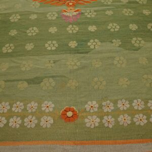Close-up of a green rug featuring scattered yellow flowers and a prominent border of white and orange blooms.