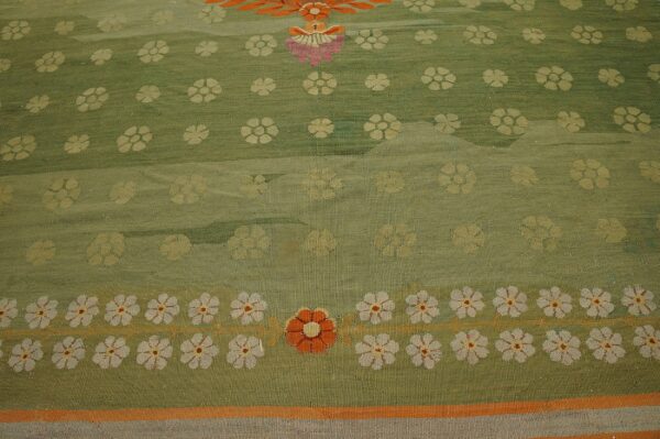 Close-up of a green rug featuring scattered yellow flowers and a prominent border of white and orange blooms.