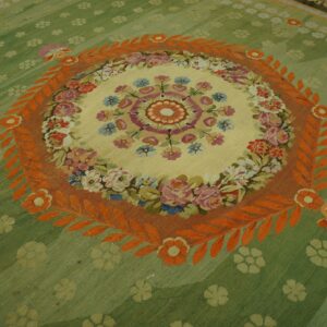 Sage green rug featuring a central floral medallion in cream, framed by a striking orange leaf border.