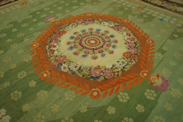 Sage green rug featuring a central floral medallion in cream, framed by a striking orange leaf border.