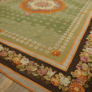 Green floral rug with a dark brown border featuring large pink and orange roses on hardwood flooring.