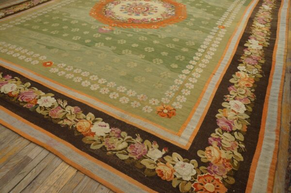 Green floral rug with a dark brown border featuring large pink and orange roses on hardwood flooring.