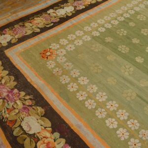 Sage green rug with dark brown floral borders and white daisy patterns rests on light wooden plank floors.