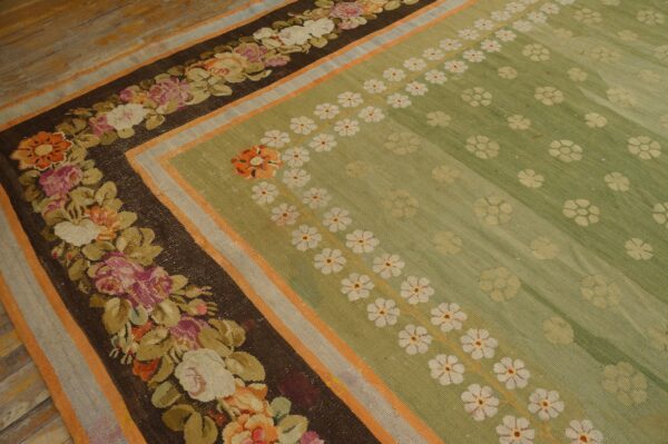 Sage green rug with dark brown floral borders and white daisy patterns rests on light wooden plank floors.