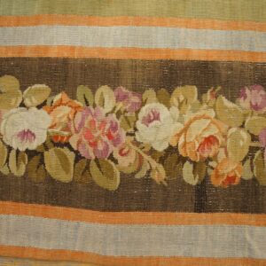 Low-pile rug with a central dark brown floral garland featuring pink, cream, and orange, surrounded by striped borders.
