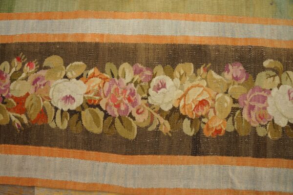 Low-pile rug with a central dark brown floral garland featuring pink, cream, and orange, surrounded by striped borders.