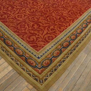 Red floral pattern rug with a wide tan border featuring blue and pink chain-link designs on wood plank flooring.