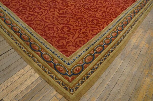Red floral pattern rug with a wide tan border featuring blue and pink chain-link designs on wood plank flooring.