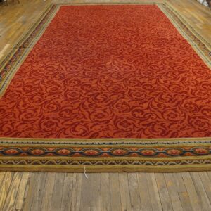 Expansive orange rug with dense red scrollwork pattern and complex gold, blue, and olive borders on wood flooring.
