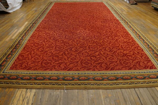 Long red rug with a tone-on-tone scrolling pattern and complex olive-and-blue border on wood floors.