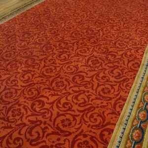 Red damask patterned rug with a wide gold and blue medallion border lying on wood flooring.
