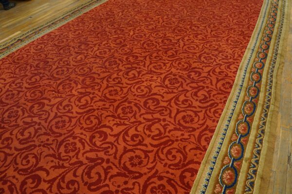 Red damask patterned rug with a wide gold and blue medallion border lying on wood flooring.