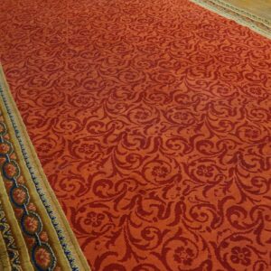 Red scrolling floral rug with a wide gold border featuring blue and coral circles on wood floor.