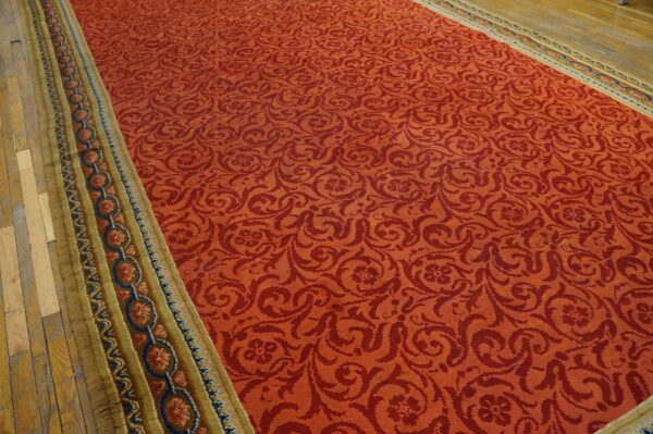 Red scrolling floral rug with a wide gold border featuring blue and coral circles on wood floor.