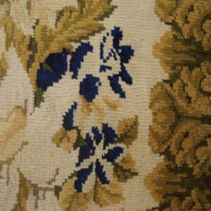 Close detail of a thick floral rug in beige, gold, and blue colors against plank wood flooring.