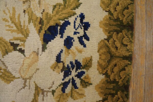Close detail of a thick floral rug in beige, gold, and blue colors against plank wood flooring.
