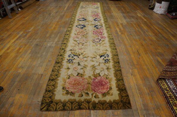 Ivory floral runner rug with pink and blue flowers and a dense green border on distressed hardwood floor.