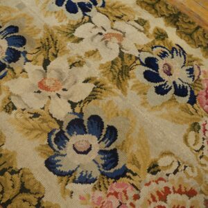 Low-pile rug displaying large blue, cream, and pink floral patterns among olive green leaves on a wood floor.