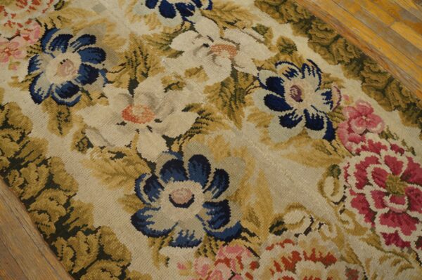 Low-pile rug displaying large blue, cream, and pink floral patterns among olive green leaves on a wood floor.