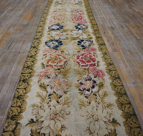 Textured runner with multicolor botanical design and olive green trim laid over distressed gray floorboards.