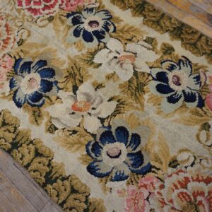 Detailed view of a dense floral rug in blue, pink, and gold over distressed gray wood flooring.