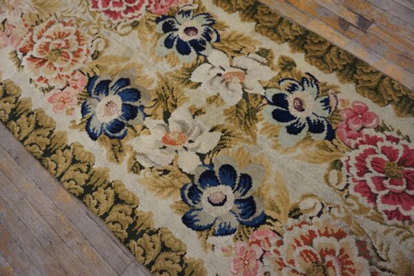Detailed view of a dense floral rug in blue, pink, and gold over distressed gray wood flooring.