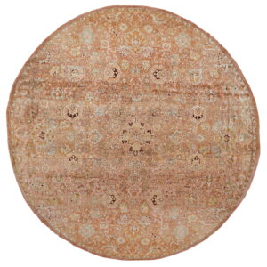 A circular rug displays a distressed traditional floral design dominated by soft peach and cream colors.