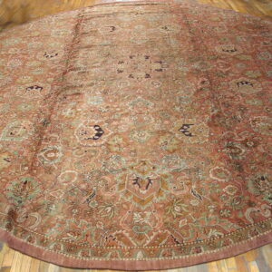 A circular low-pile rug featuring a dense terracotta and sage floral pattern rests on wood plank flooring.