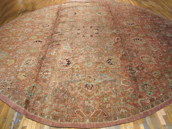 A circular low-pile rug featuring a dense terracotta and sage floral pattern rests on wood plank flooring.