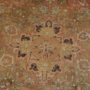 Intricate traditional rug pattern featuring a central medallion and floral motifs in dusty pink, green, and brown.