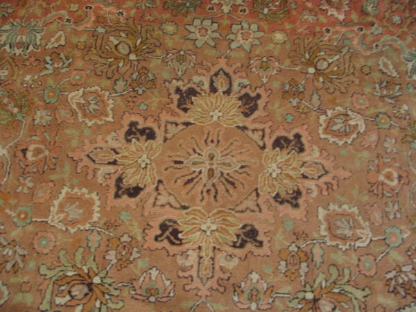 Intricate traditional rug pattern featuring a central medallion and floral motifs in dusty pink, green, and brown.