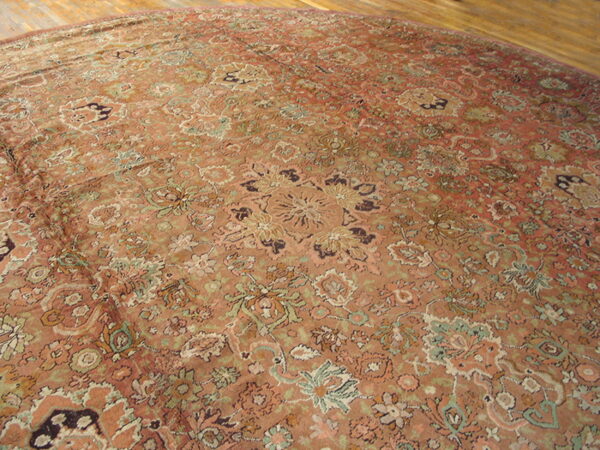 Round low-pile rug with a dense faded floral pattern in terracotta, green, and cream on wooden floors.