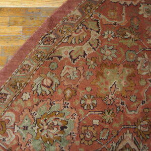 Dusty red floral rug featuring sage green and gold accents rests on worn hardwood flooring.