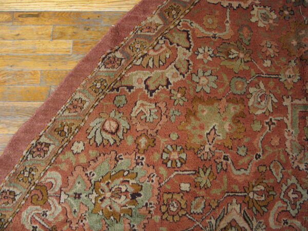 Dusty red floral rug featuring sage green and gold accents rests on worn hardwood flooring.