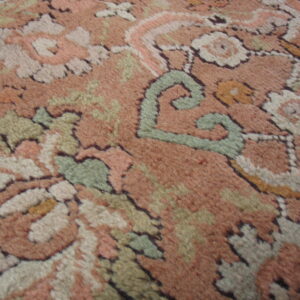 Plush pile close-up of a traditional floral rug pattern featuring dusty rose, cream, and sage green motifs.