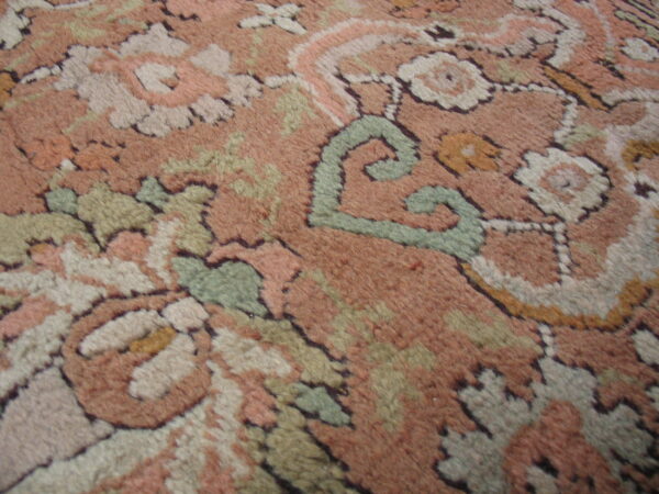 Plush pile close-up of a traditional floral rug pattern featuring dusty rose, cream, and sage green motifs.