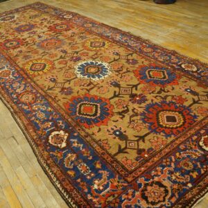 Colorful low-pile rug with red, blue, and yellow floral patterns on a camel field on worn plank flooring.